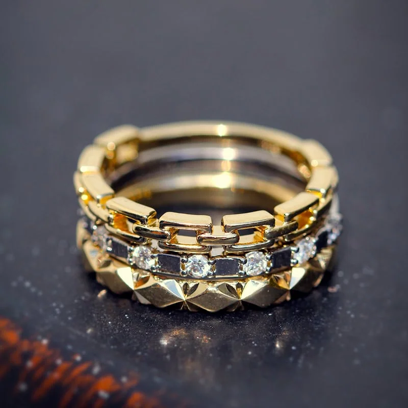 Stacked gold rings featuring a chain-link band, diamond band, and textured gold band