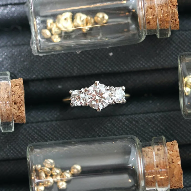 Three-stone diamond engagement ring surrounded by small vials of gemstones