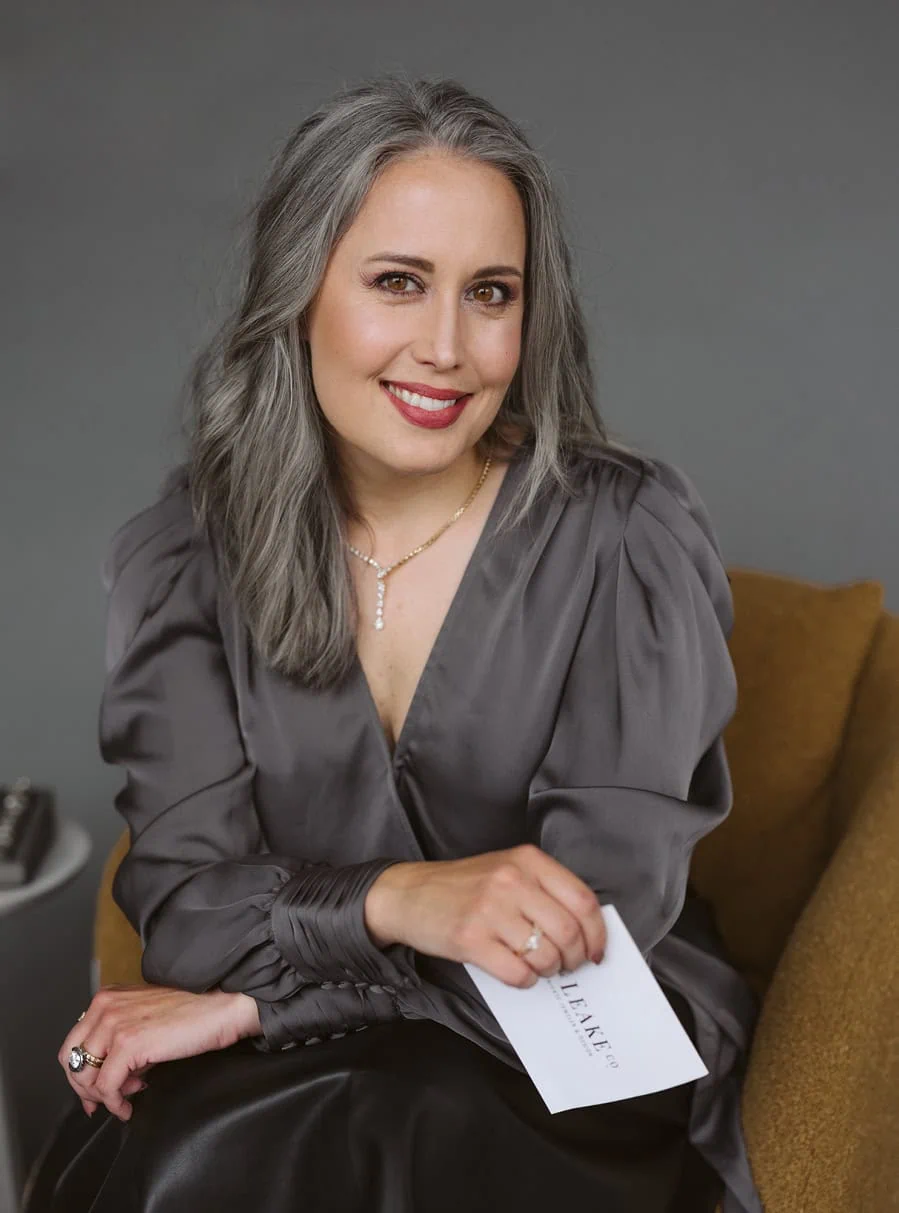 Jewelry designer, Sarah Rowe, wearing diamond necklace and ring, seated and smiling