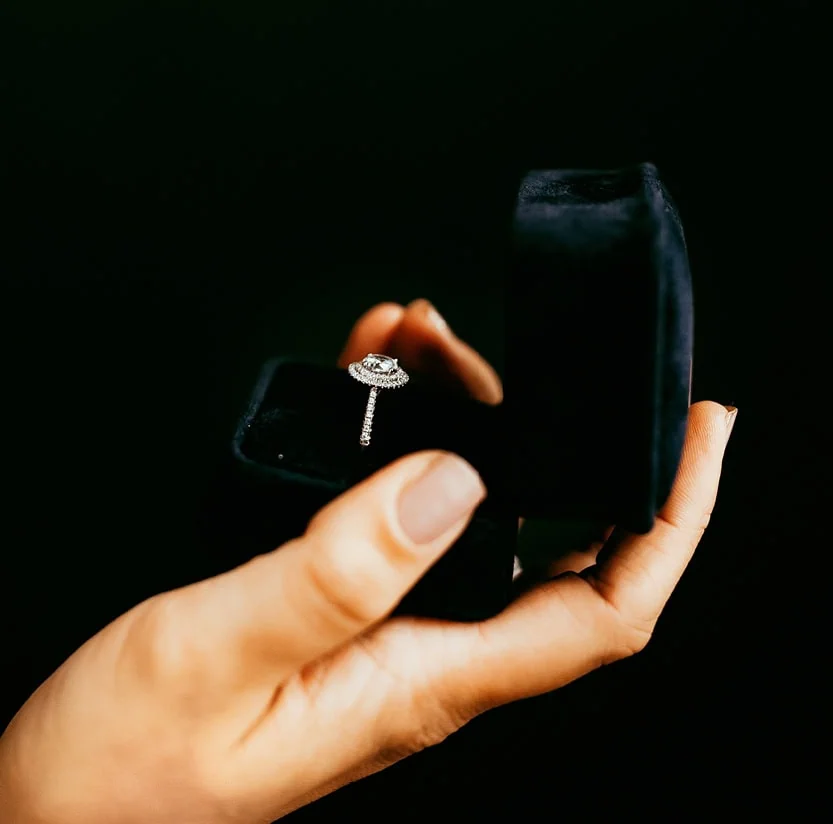 Hand holding an engagement ring in a black ring box