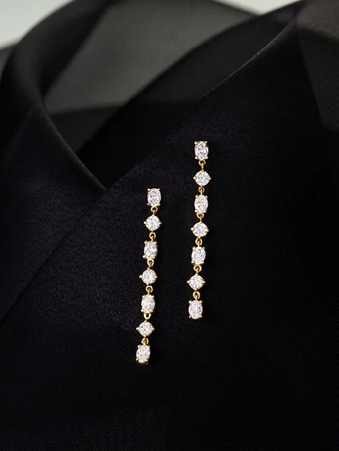 Gold drop earrings with diamonds displayed on black fabric