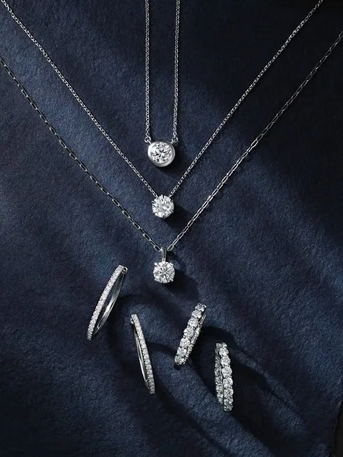 Diamond pendant necklaces and diamond hoop earrings displayed on a dark background