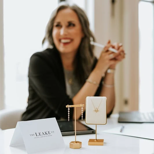 Jewelry designer sitting at a desk with necklace and earring displays