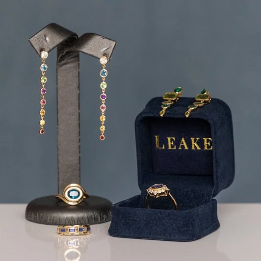 Jewelry display featuring colorful drop earrings, rings, and a ring in a Leake jewelry box