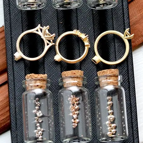 Ring settings and small gemstones displayed in glass bottles on a jeweler’s tray