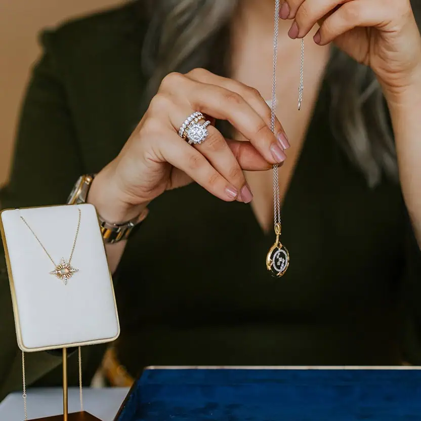 Jewelry designer holding a custom pendant necklace while reviewing fine jewelry pieces at The Leake Co. in Louisville, Kentucky